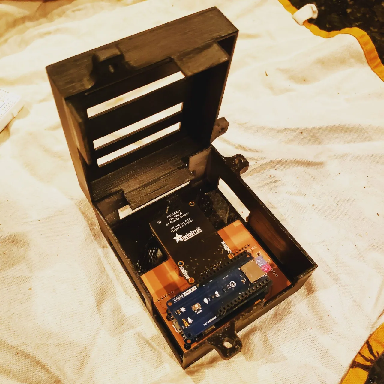 An open-source air quality monitor: a 3D-printed enclosure housing an Adafruit PM2.5 sensor mounted above an Arduino MKR board