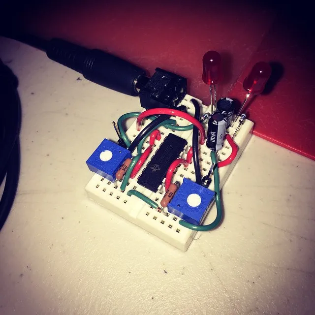 An early breadboard prototype with an integrated circuit, two blue trimpots, red LEDs, resistors, and a barrel-jack power connector