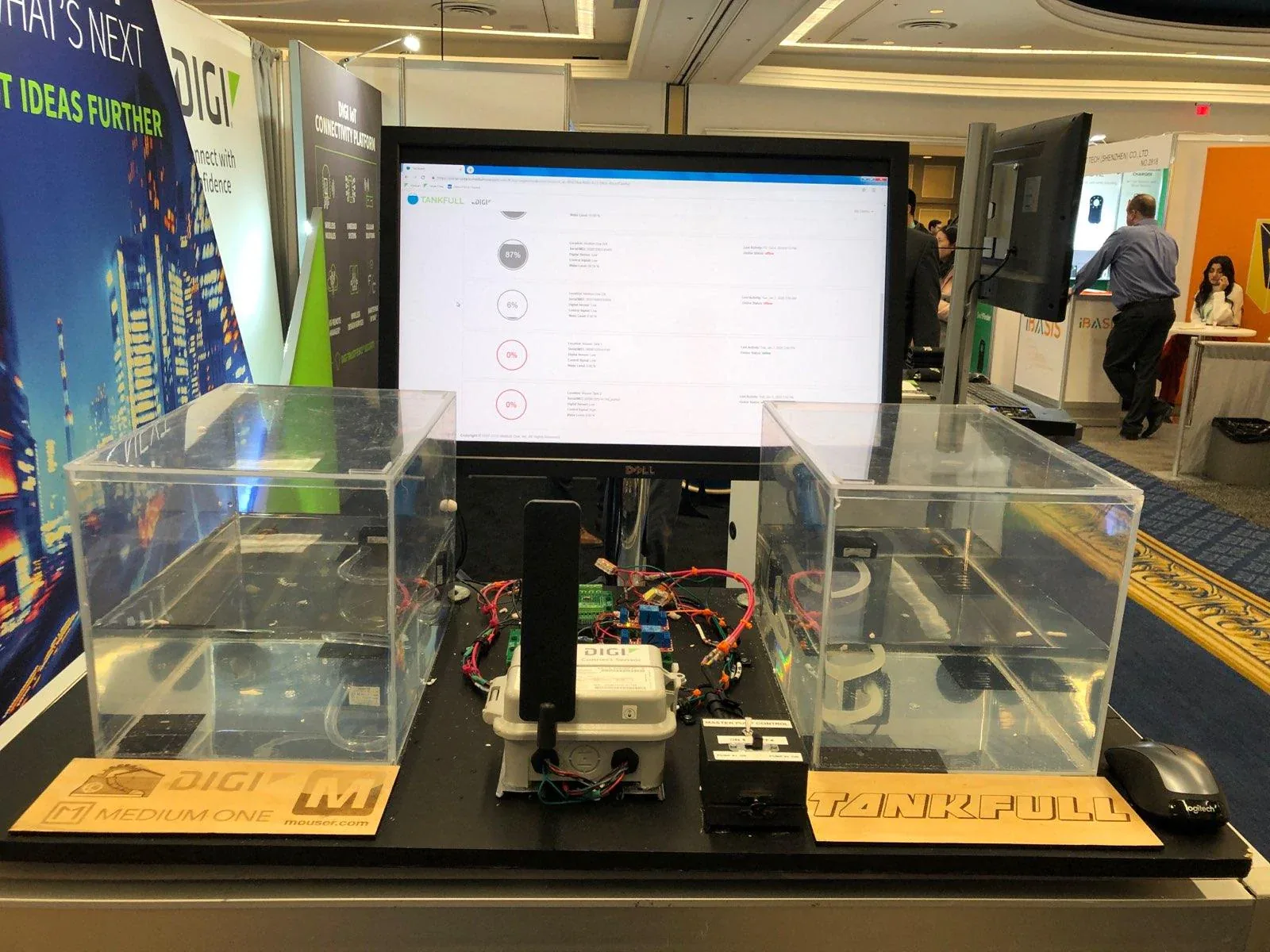 The TANKFULL exhibit on the CES show floor: two clear acrylic tanks wired to a Digi Connect Sensor, with a live TANKFULL dashboard on the monitor behind, branded Digi, Medium One, and Mouser